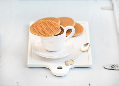 Dutch caramel stroopwafels and cup of black coffee on white ceramic serving board over light blue wooden backdrop