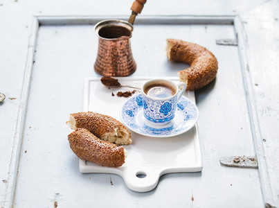 Turkish black coffee served in traditional ceramic cup with pattern  sesame bagel called simit on white serving board over light blue wooden background
