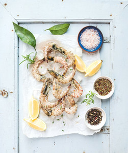 Fresh uncooked shrimps with lemon herbs ice and spices on rustic blue wooden board backdrop
