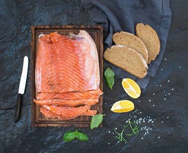 Smoked salmon filet with lemon  fresh herbs and bred on wooden serving board over dark stone backdrop