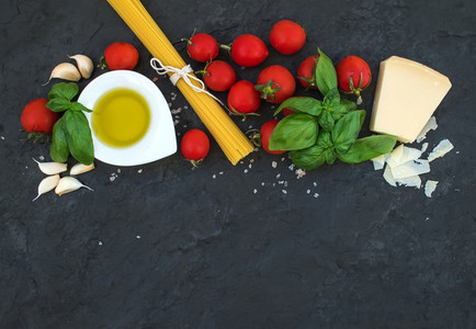 Ingredients for cooking pasta Spaghetti olive oil garlic Parmesan cheese tomatoes and fresh basil on black slate background top view copy space