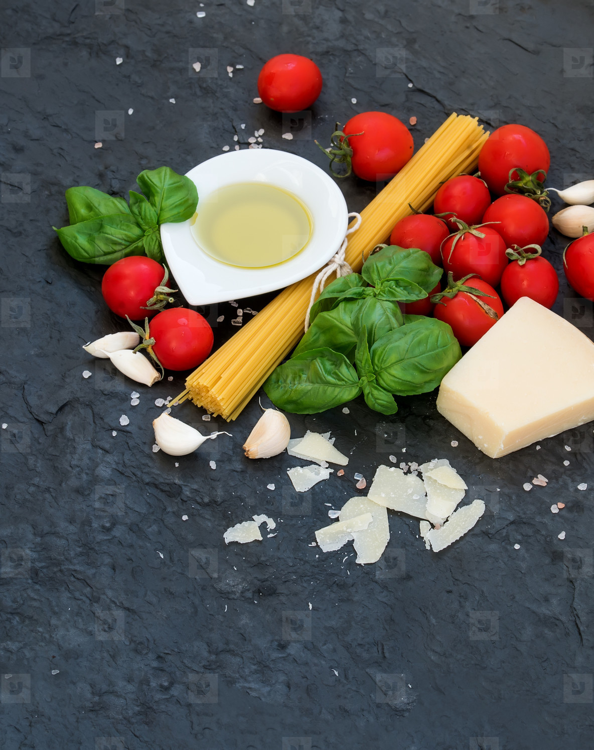 Ingredients for cooking pasta. Spaghetti, olive oil, garlic, Parmesan cheese, tomatoes and fresh basil on black slate background, top view, copy space.