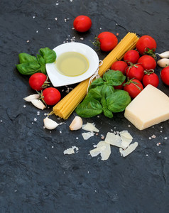 Ingredients for cooking pasta  Spaghetti  olive oil  garlic  Parmesan cheese  tomatoes and fresh basil on black slate background  top view  copy space