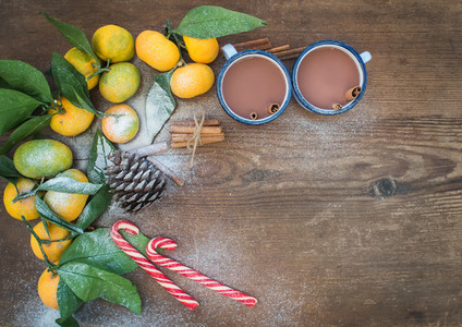 Christmas or New Year frame  Fresh mandarins with leaves  cinnamon sticks  pine cone  hot chocolate in mugs and candy canes over rustic wooden background  top view
