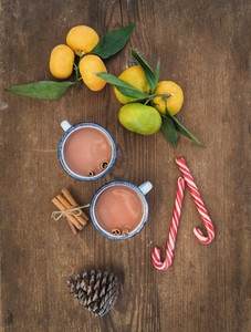 Christmas or New Year attributes  Fresh mandarins with leaves  cinnamon sticks  pine cone  hot chocolate in mugs and candy canes over rustic wooden background  top view
