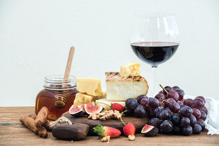 Glass of red wine  cheese board  grapes fig  strawberries  honey and bread sticks  on rustic wooden table  white background