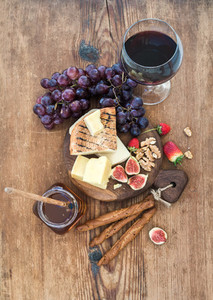Glass of red wine cheese board grapesfig strawberries honey and bread sticks  on rustic wooden table