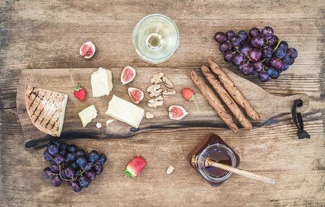 Glass of white wine cheese board grapes figs strawberries honey and bread sticks on rustic wooden background