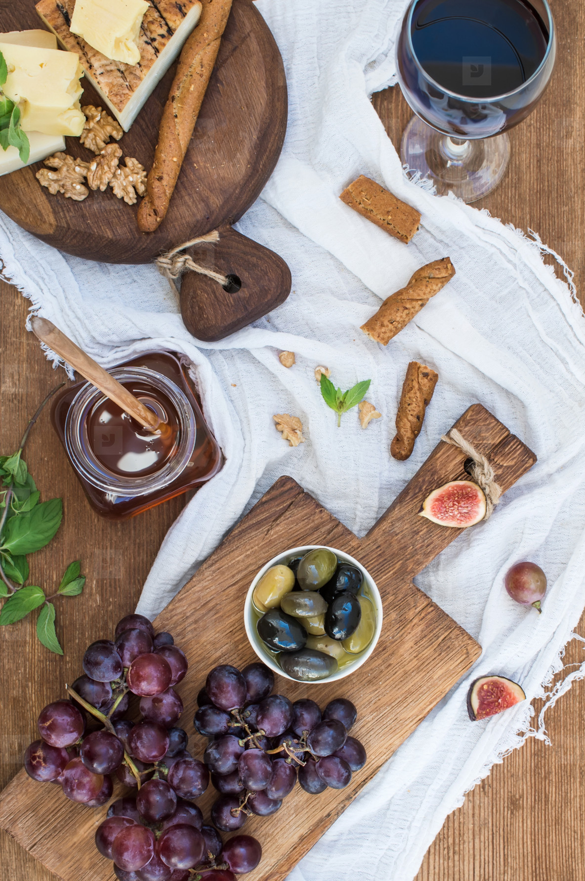 Glass of red wine  cheese board  grapes  walnuts  olives  honey and bread sticks on rustic wooden table
