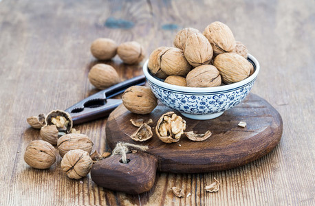 Walnuts in ceramic bowl and on cutting board with nutcracker over  rustic wooden background
