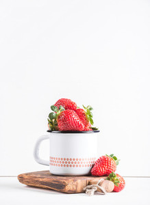 Fresh ripe red strawberries in country style enamel mug on rustic wooden board over white background