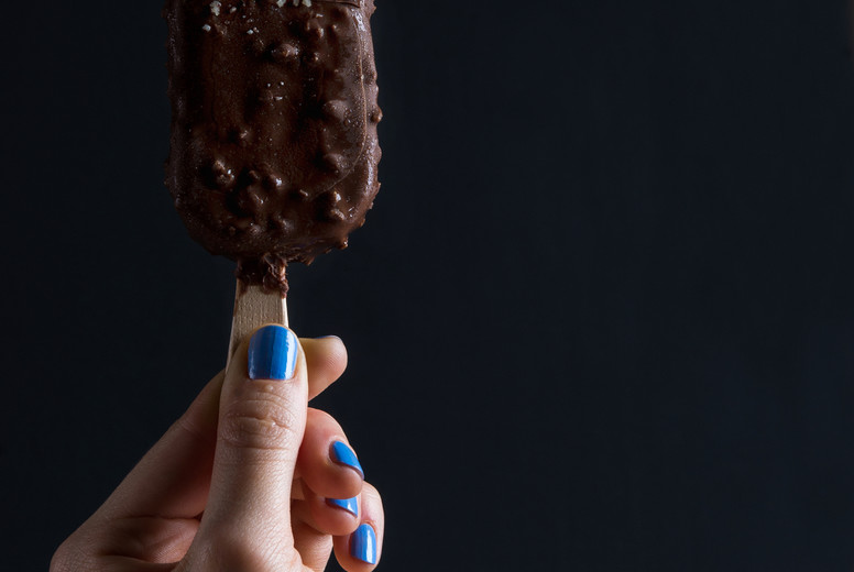 Chocolate dipped popsicle ice cream with chipped nuts held by woman's hand on black