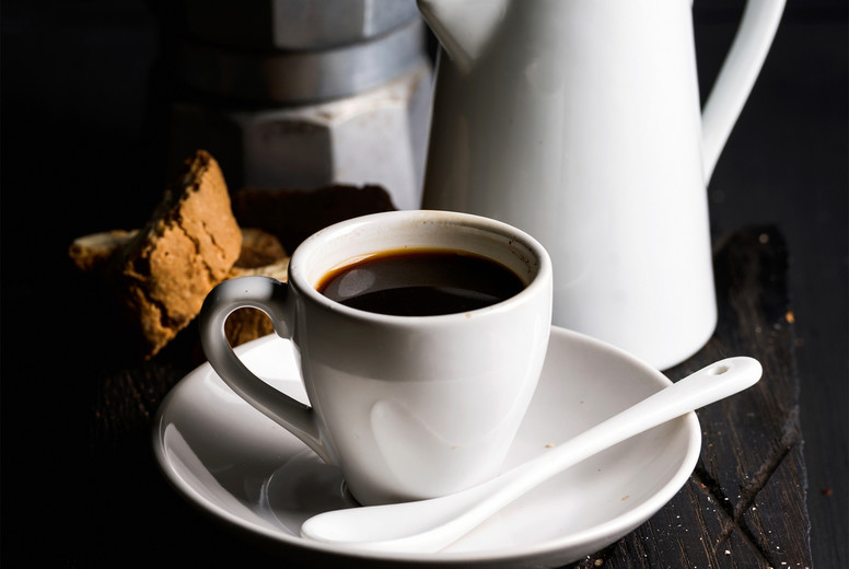 Cup of hot espresso, creamer with milk, cantucci and moka coffee pot on a rustic wooden board