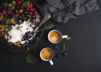Healthy breakfast  Oat granola crumble with fresh berries  seeds and ice cream in iron skillet pan on dark wooden board over black backdrop
