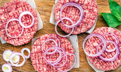 Raw ground beef meat cutlet for making burgers with onion rings and spices on wooden background