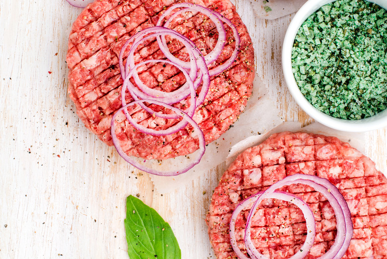 Raw ground beef meat cutlet for making burgers with onion rings and spices on white wooden background