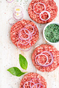 Raw ground beef meat cutlet for making burgers with onion rings and spices on white wooden background