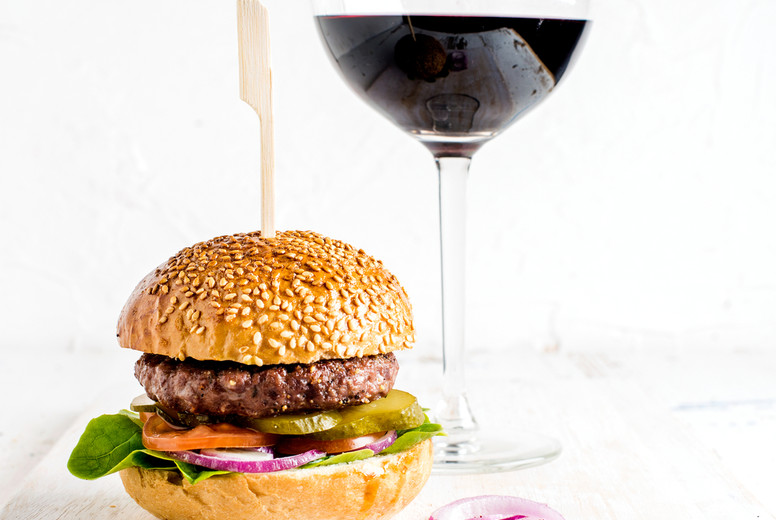 Fresh homemade burger on wooden serving board with onion rings and glass of red wine