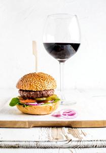 Fresh homemade burger on wooden serving board with onion rings and glass of red wine