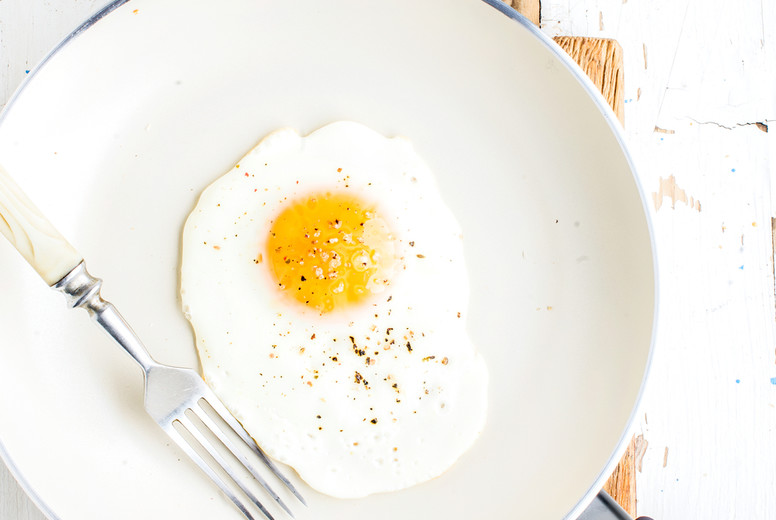 Fried egg with spice and bread slices in white ceramic frying pan on wooden board 