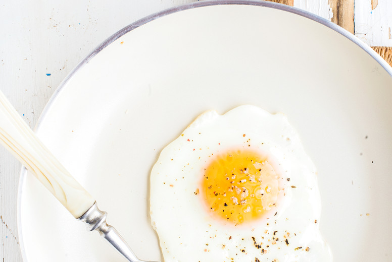 Fried egg with spice and bread slices in white ceramic frying pan on wooden board 