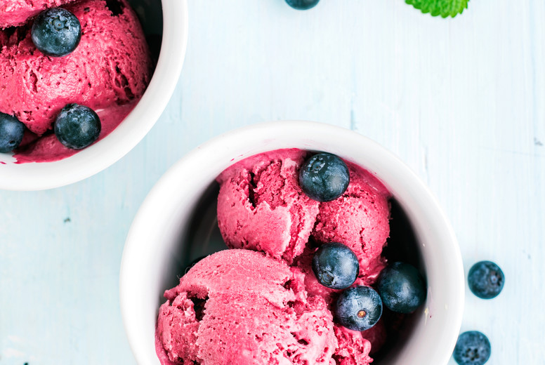 Homemade blueberry ice cream scoops with fresh berries and mint leaves in cups over light blue background
