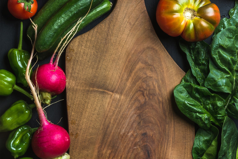 Fresh raw ingredients for healthy cooking or salad making with dark wooden cutting baoard in center, top view, copy space
