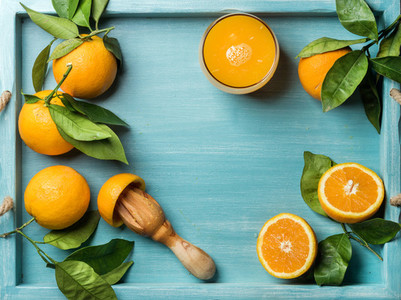 Fresh orange juice in glass and oranges with leaves on wooden turquoise blue painted background