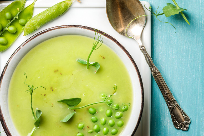 Light summer green pea cream soup in bowl with sprouts, bread toasts and spices