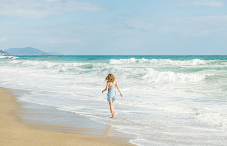 Young woman in blue denim jumpsuit walking to the sea