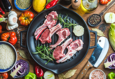 Ingredients for cooking healthy meat dinner Raw uncooked lamb chops in iron grill pan with vegetables rice herbs and spices over rustic wooden background