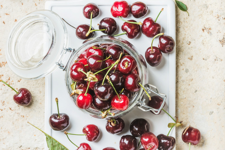 Sweet cherry in glass jar on white board over concrete background