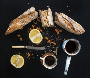 Rustic breakfast set of french baguette broken into pieces grapefruit sunflower seeds almonds and coffee on dark