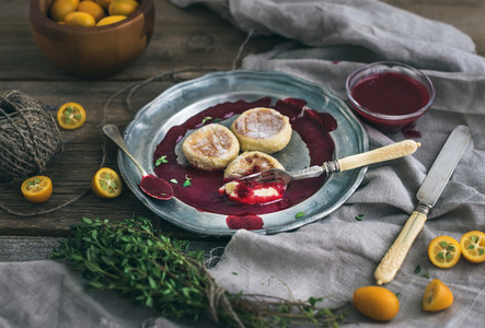 Rustic breakfast set  Russian cheese cakes on a vintage metal plate with lingonberry jam  fresh kumquats  thyme  decoration rope and old dinnerware over rough wooden desk