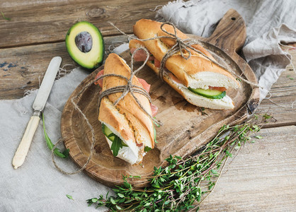 Salmon avocado and thyme sandwiches in baguette tied up with decoration rope on a rustic wooden board over rough wood background