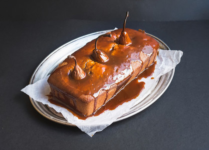Spicy pear cake with caramel topping on a silver dish on a dark
