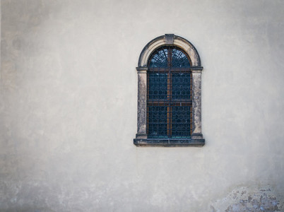 Antique medieval window with iron bars and old white wall
