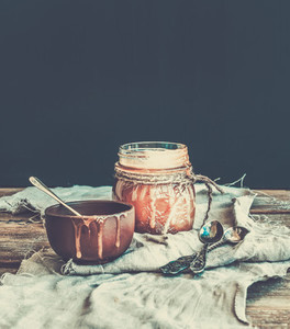 Salted caramel sauce in a rustic glass jar and brown ceramic cup on wooden desk