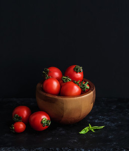 Ripe cherry tomatoes in wooden bowl with basil leaves spices and salt
