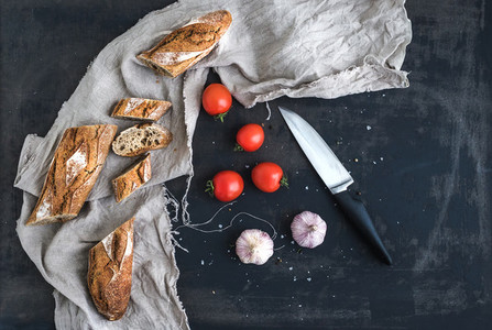 French baguette cut into pieces cherry tomatoes garlic and kitchen knife over dark grunge background