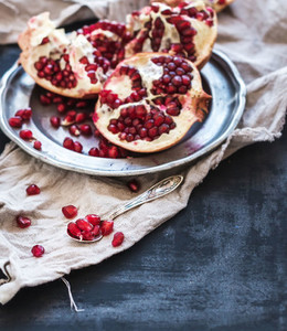 Red ripe peeled pomegranate on rustic metal plate and beige kitchen towel over dark background