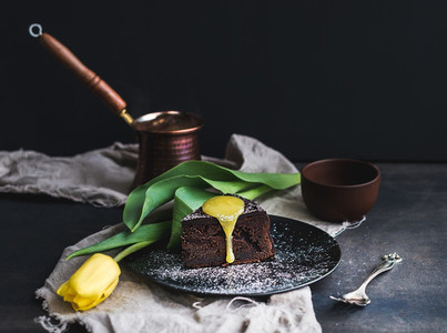 Perfect morning set for woman Piece of truffle chocolate cake with lemon curd icing hot coffee and yellow tulip on dark backdrop