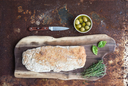 Freshly baked homemade ciabatta bread with olives  basil and thyme on walnut wood board over grunge rusty metal background  top view