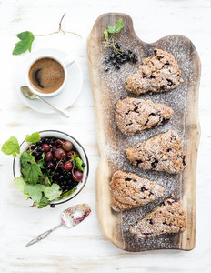 Fresh black currant scones with coffee and bowl of berries over rustic walnut wood serving board top view