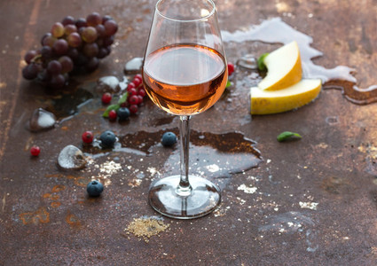 Glass of rose wine with berries melon grapes and ice on grunge rusty metal background