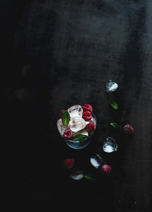 Ice cubes with mint leaves and raspberry in glass on dark grunge surface