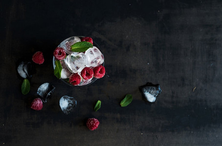 Ice cubes with mint leaves and frozen raspberry in glass on grunge dark background