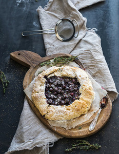 Homemade crusty pie or galette with blueberries thyme and ice cream on rustic wooden board over dark backdrop