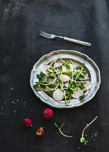 Spring salad with sunflower sprouts and radish in vintage metal plate over rustic dark painted background