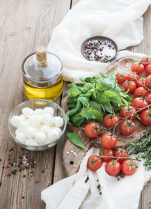 Basil  cherry tomatoes  mozarella  olive oil   salt  spices on rustic chopping board over old wood background